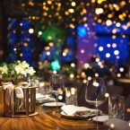 Blurred background of restaurant, bar or night club with colorful lights bokeh. Abstract defocused blur background. Selective focus. Christmas dinner, festive table setting with flowers decorations.